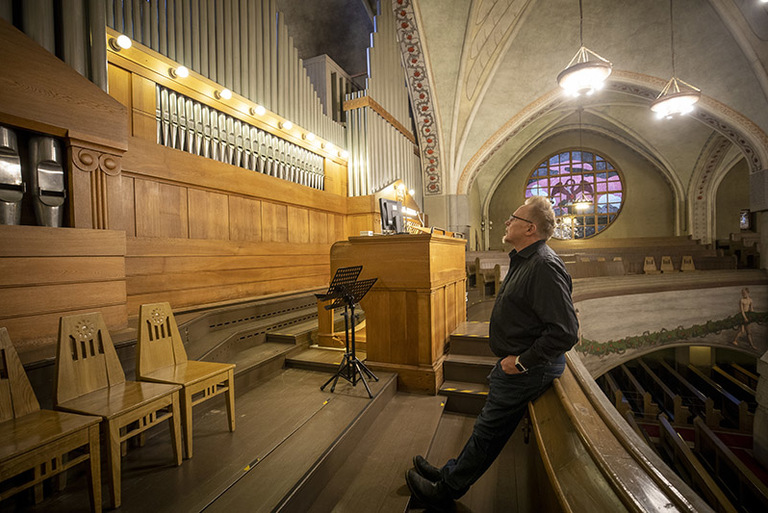 Mies istuu kaiteen reunalla kädet taskuissa ja katselee urkuja kirkossa.